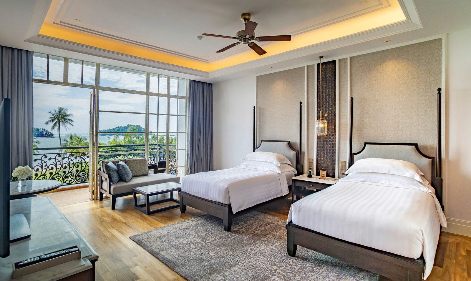 Twin-bed hotel suite with full-height glazing opening to a sea-facing balcony
