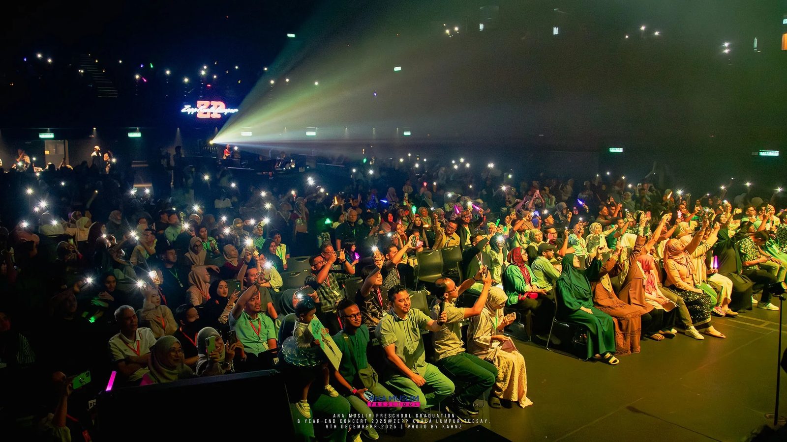 Outdoor night audience lit by phone screens and stage beams