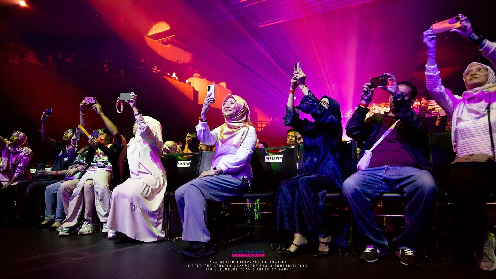 Cast celebrating together on stage under magenta lighting