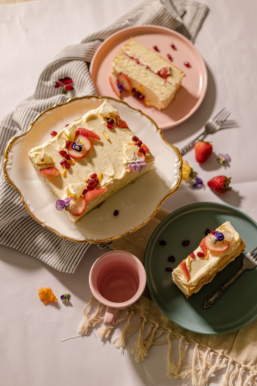 Layered cake with strawberries and edible flowers, styled flatlay on linen