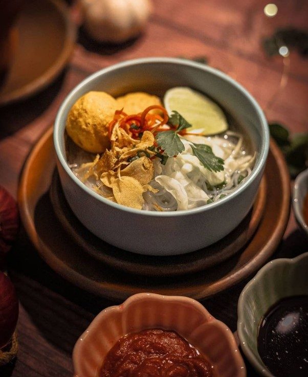 Noodle soup bowl with lime, coriander and crisp shallots on a timber table