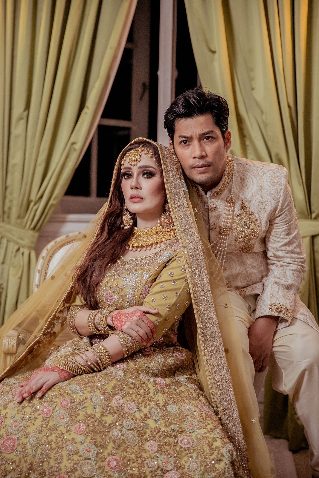 Couple in gold traditional dress seated beside draped curtains