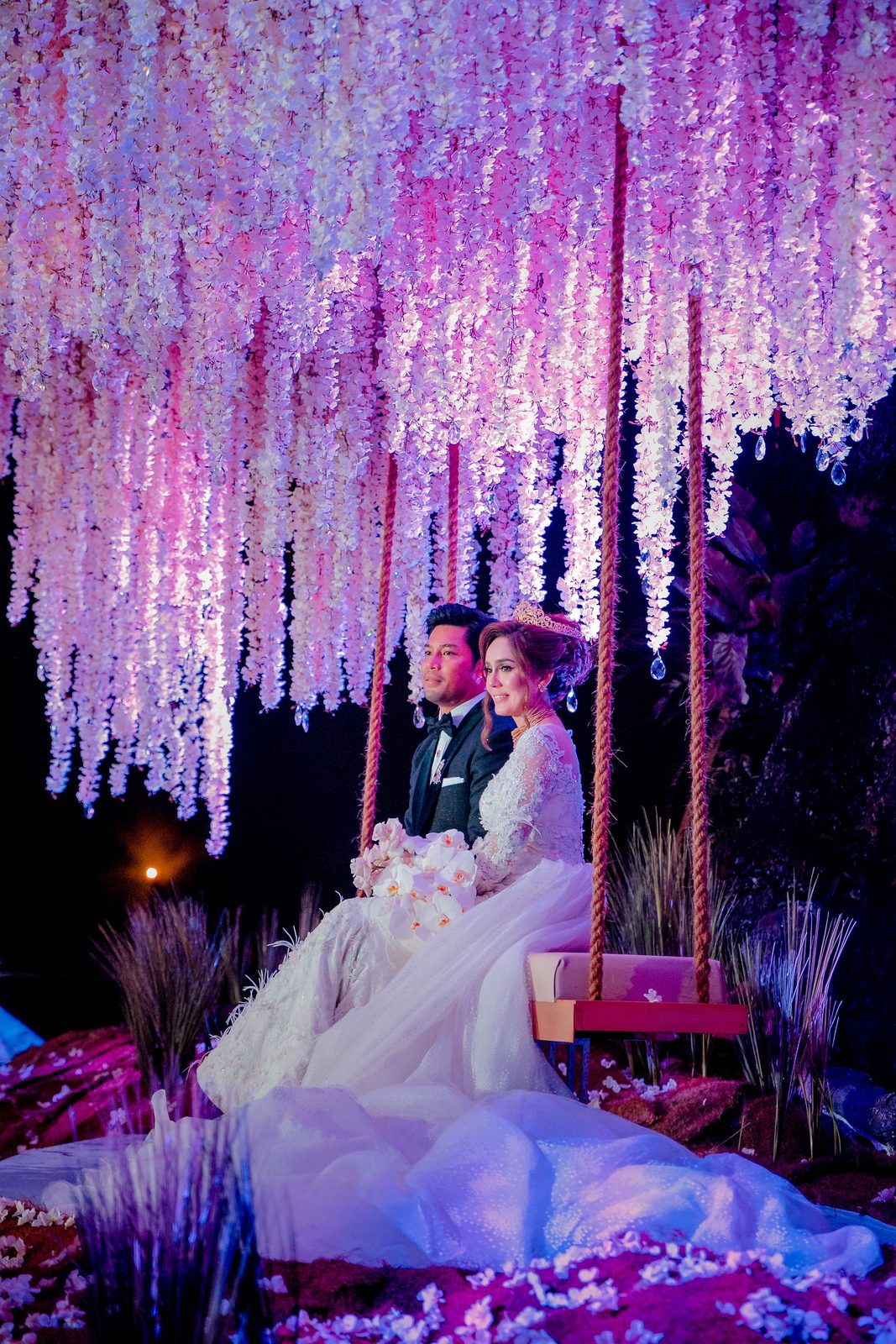 Bride seated on a decorated swing beneath a cascading floral installation
