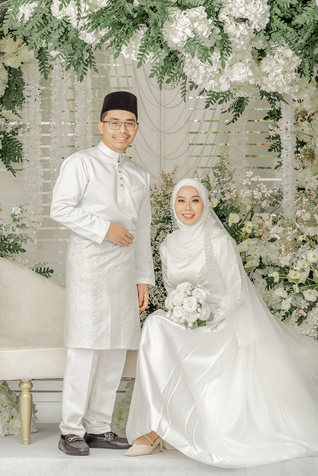 Couple in white standing beside a white floral arch